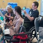 Photo of attendees, some in wheelchairs or with other adaptive equipment, working on their paintings at a June 2024 "This Is Your Brain On Art" Guided Workshop