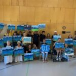 Photo of a group of people, some in wheelchairs or with other adaptive equipment, holding up their finished paintings from a June 2024 "This Is Your Brain On Art" Guided Workshop